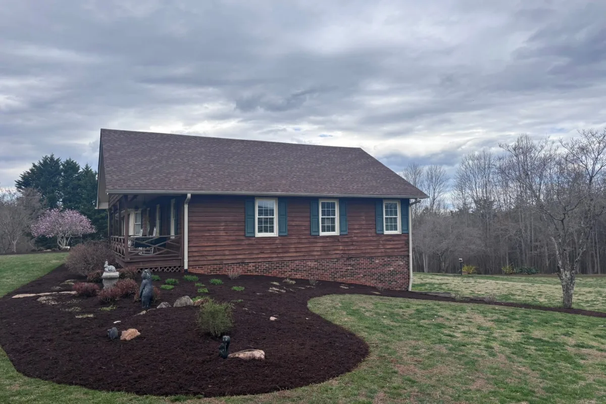 Fresh mulch beds with small plantings beside a cedar-sided house